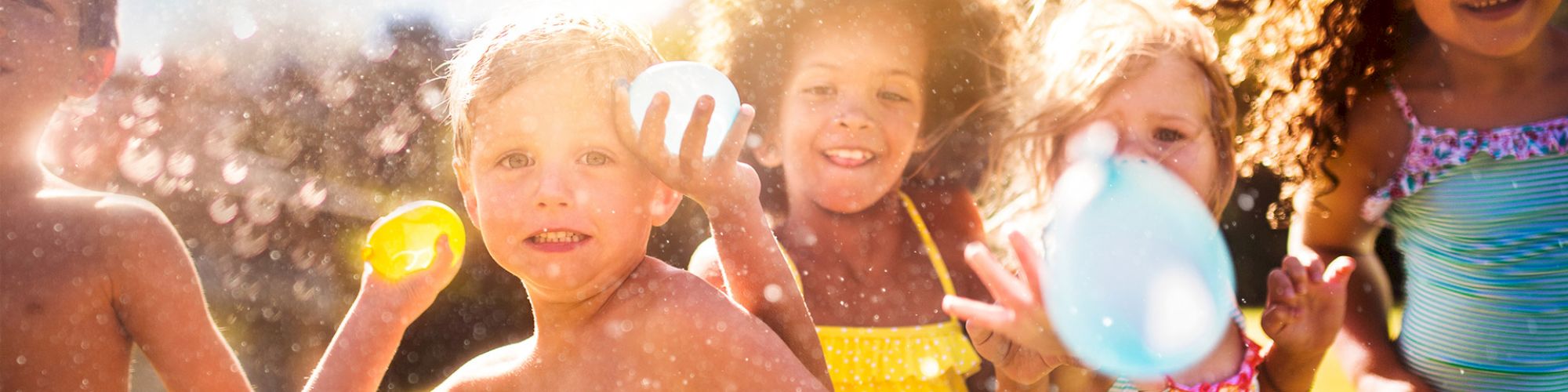 Children having fun with water balloons in a sunlit outdoor setting, smiling and playing together in colorful swimsuits.
