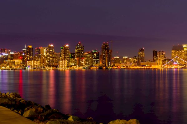 This image shows a city skyline at night, with buildings illuminated and their reflections shimmering on the water.