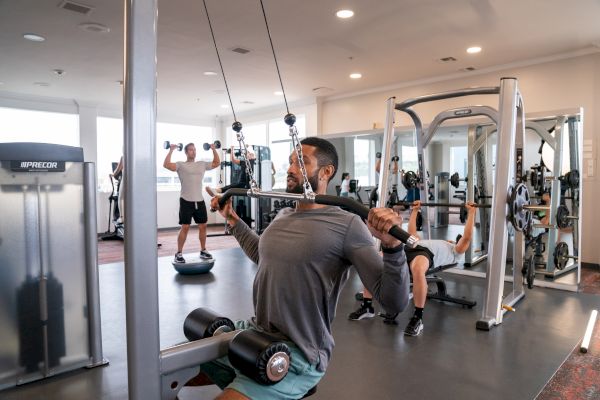People are working out in a gym using various equipment, including cable machines, free weights, and benches.