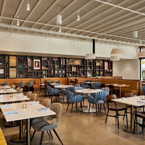 This image shows a modern, stylish dining area with multiple tables, chairs, and a long yellow bench. Shelves with decor line the back wall.