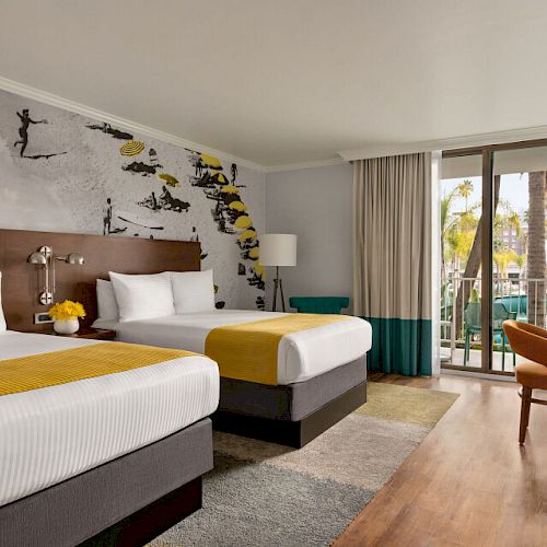 A hotel room with two beds, yellow accents, a wall mural, a balcony with a view, a desk, and a TV on a dresser.
