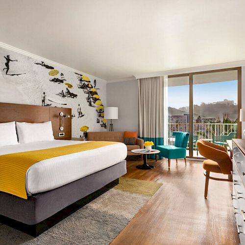 A modern hotel room with a large bed, armchairs, a TV, and wall art featuring skiers. The room has a balcony with a view of a landscape.