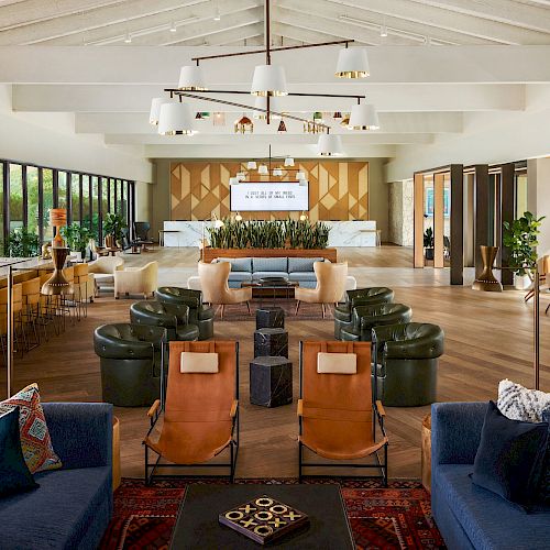 The image shows a spacious, modern lounge area with various seating options, a bar on the left, and large windows providing natural light.