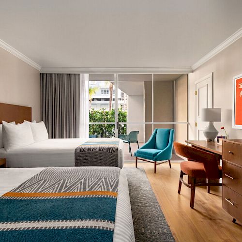 A modern hotel room features two beds, a flatscreen TV on a wooden dresser, a desk with a chair, and a seating area with two chairs near a window.