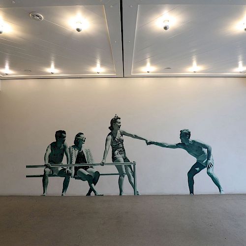 The image shows a wall mural of five people interacting, placed in a modern, well-lit room with recessed ceiling lights.