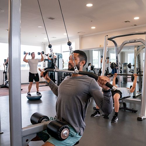 People are working out in a gym using various exercise equipment, including a weight machine, dumbbells, and a balance board.