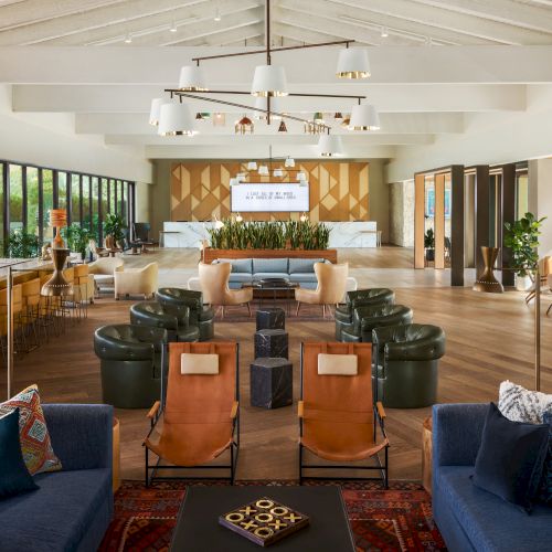 This image shows a modern hotel lobby with various seating areas, a bar, and a reception desk in the background. The decor is contemporary and inviting.