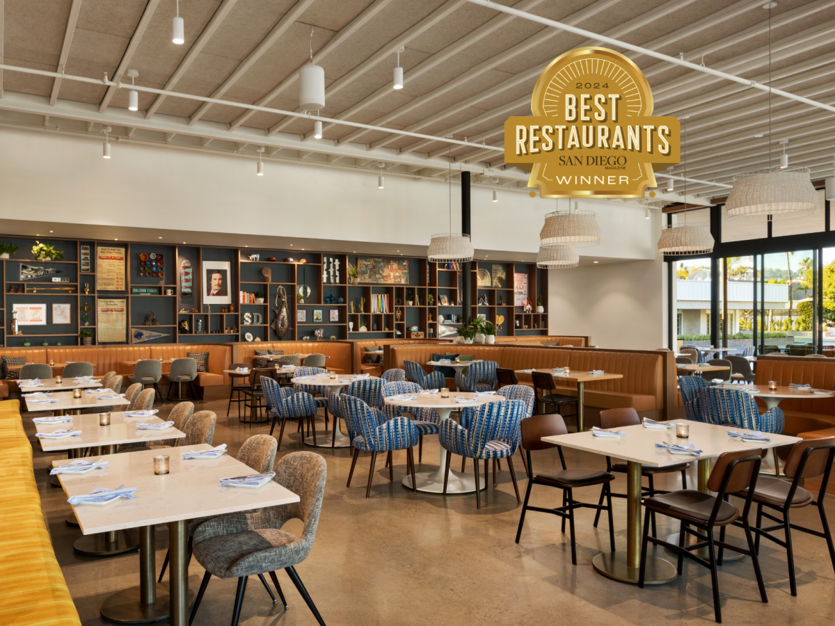 The image shows a modern restaurant interior with various seating options, a wall of books and décor, and a "Best Restaurants San Diego Winner" sign.