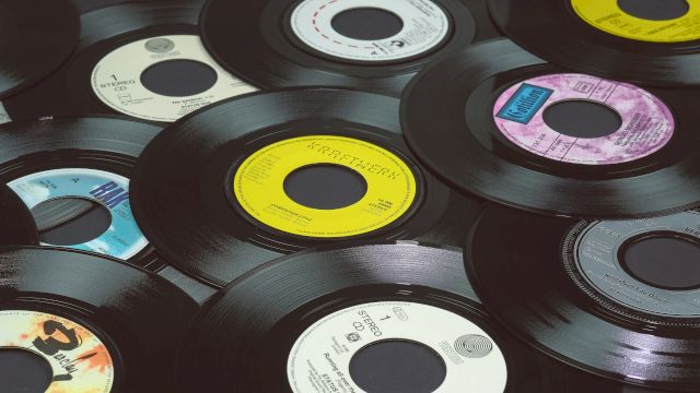 The image shows a collection of vinyl records scattered on a flat surface, each with different colored labels and designs, with black edges.