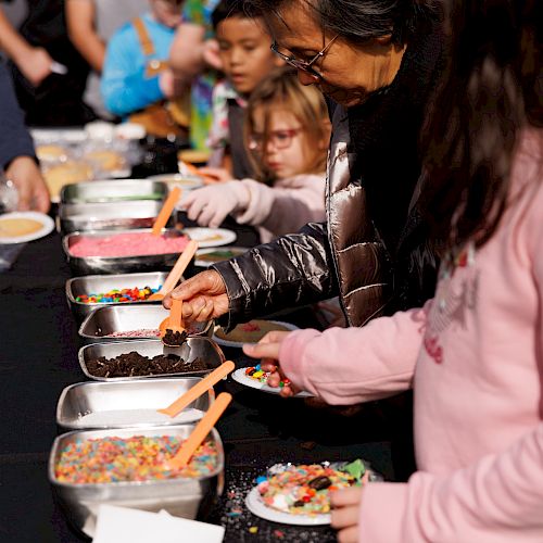 People are selecting toppings from trays for their food or desserts at a buffet-style setup.