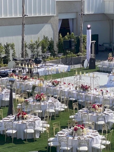 An outdoor event setup with round tables, chairs, and floral centerpieces, arranged on a green lawn with decorations.