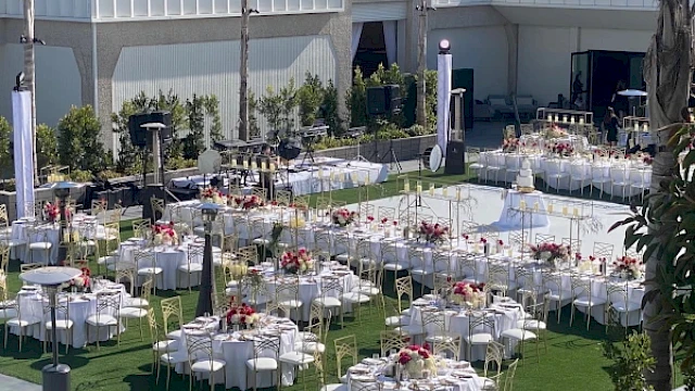 An outdoor event setup with round tables, chairs, and floral centerpieces, arranged on a green lawn with decorations.