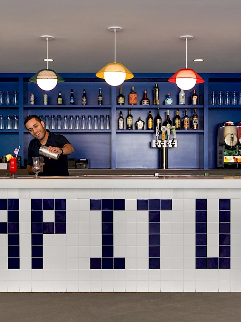 A bartender is serving drinks at a bar with "LAP IT UP" in large letters on the front.